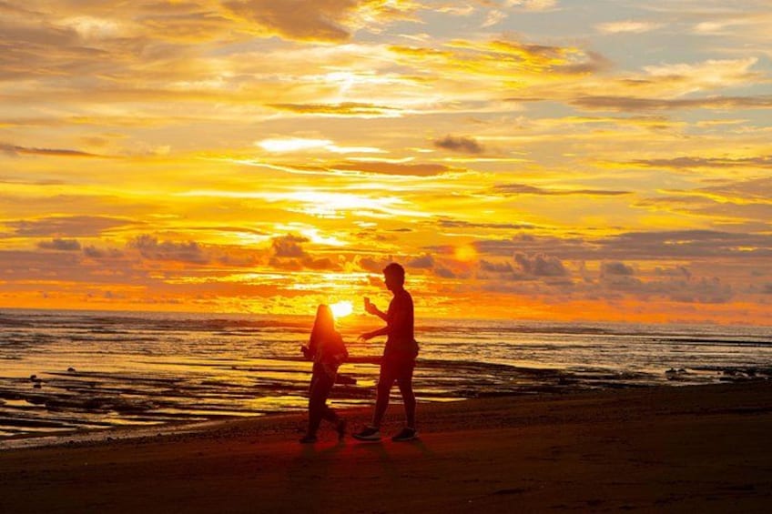 A sunset over the ocean with two silhouetted figures standing on the beach. 3