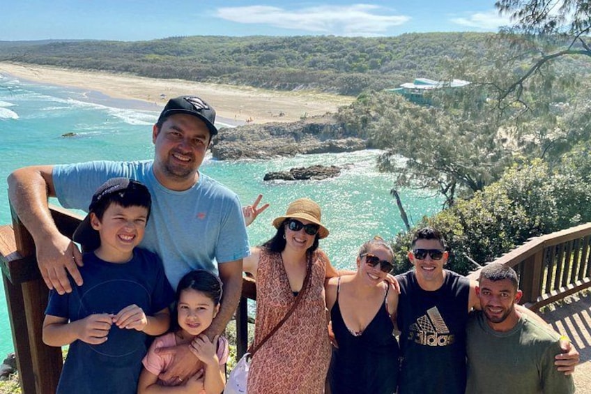 A group of people on a wooden deck overlooking a coastal landscape with trees and a beach. 2