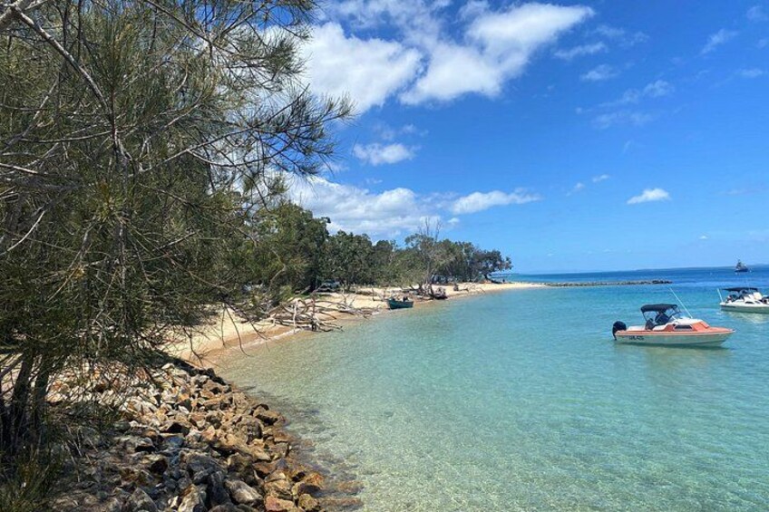 Una spiaggia con acque cristalline turchesi, un litorale roccioso e diverse imbarcazioni ancorate al largo. 2