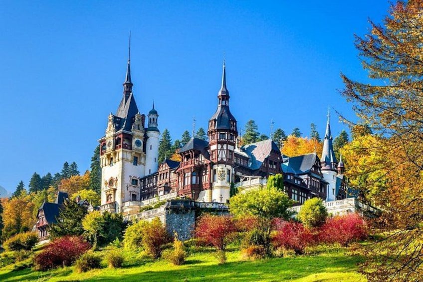 A historic castle with multiple towers and spires, surrounded by autumn-colored trees. 1