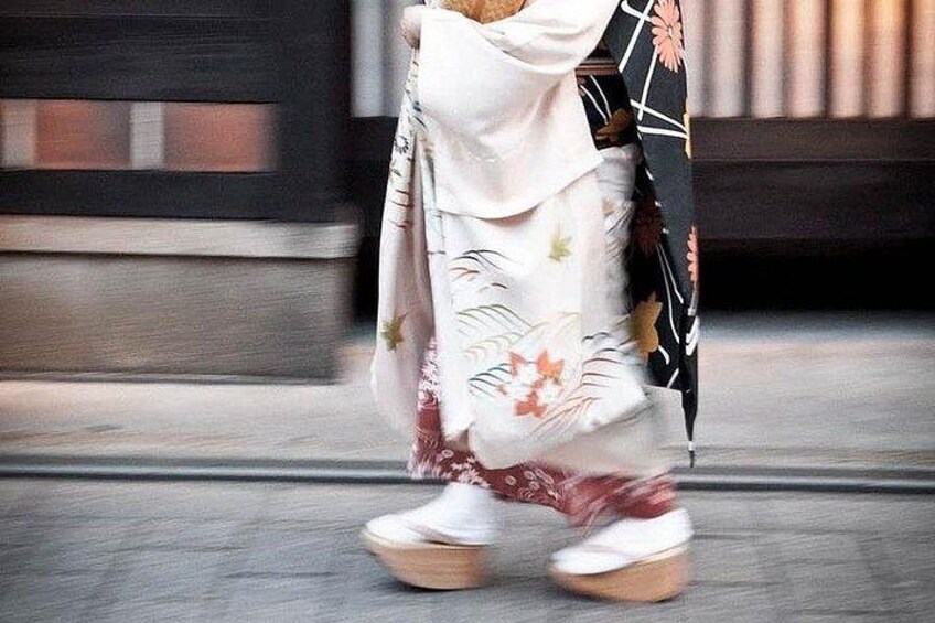 A person walking on a sidewalk wearing a floral-patterned dress and white shoes. 2