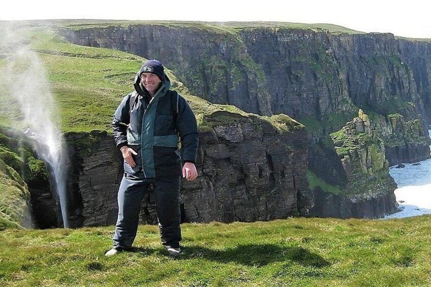 A person standing on a grassy cliff with a waterfall in the background. 4