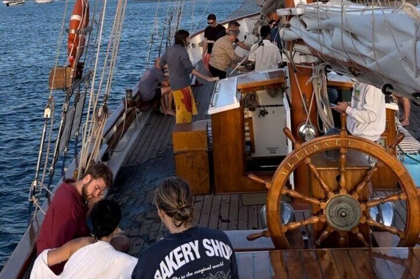 A group of people on a sailboat with a wooden wheel and a lifebuoy. 4