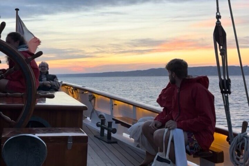 A person in a red jacket sitting on a boat deck during sunset. 3