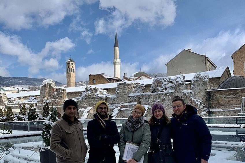 A group of people standing in a snowy urban setting with historic buildings and a prominent tower in the background. 5
