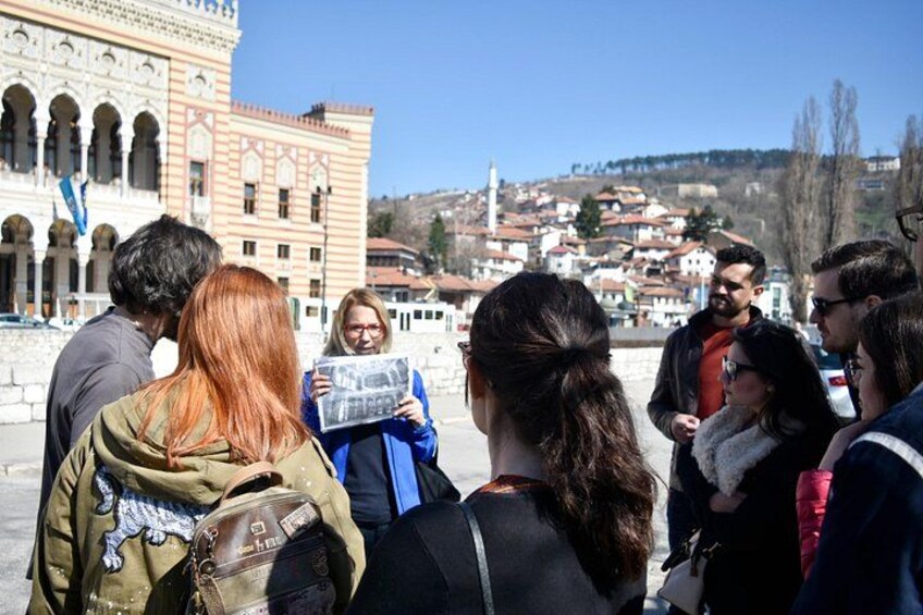 A group of people standing outdoors, some holding maps, with a historic building and a town in the background. 2