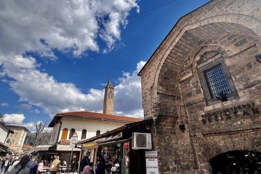 A street with a building featuring a tower, shops, and a signboard. 2