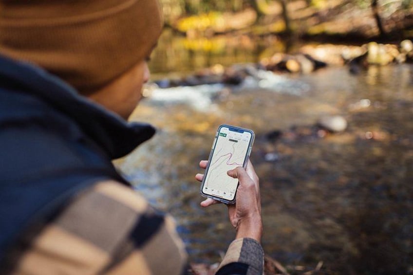 A person holding a smartphone with a map application, standing by a stream. 4
