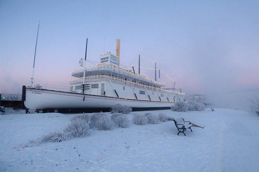 A stationary ship in a snowy landscape with a bench and bushes in the foreground. 3