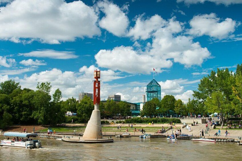 Une rivière bordée d’un monument en forme de cône, d’un bâtiment en verre et d’un parc où se promènent des gens. 2