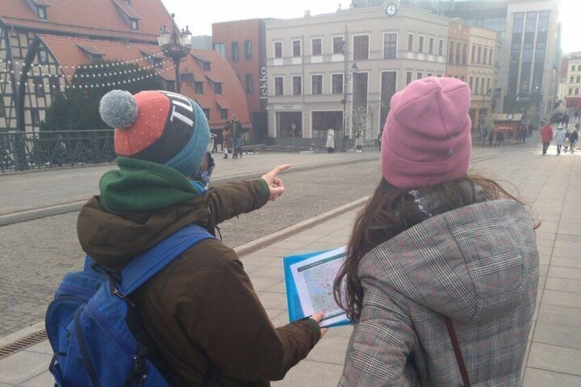 Two people looking at a map in an urban square with buildings in the background. 2