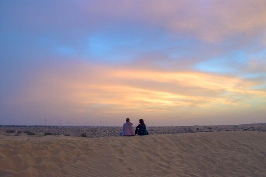 Two people sitting on a sand dune at sunset with a colorful sky. 2