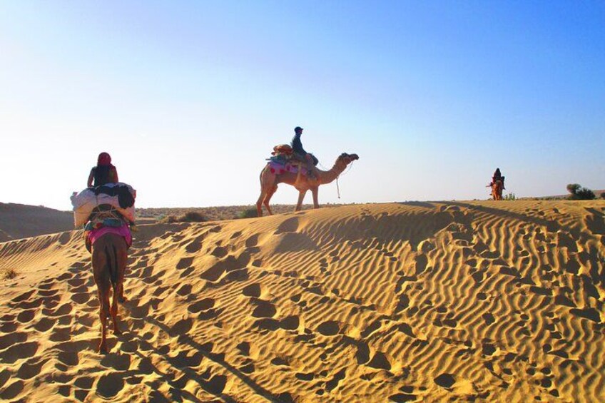 Three people riding camels on a sandy dune. 5