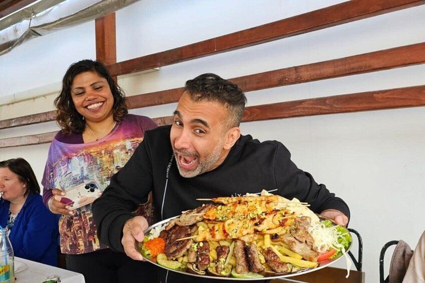 A person holding a large platter of food at a dining table. 4