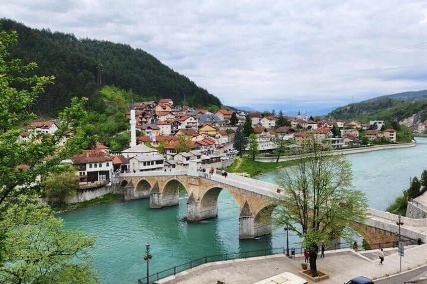 A stone bridge over a river, a town with red-roofed buildings, and green hills in the background. 1