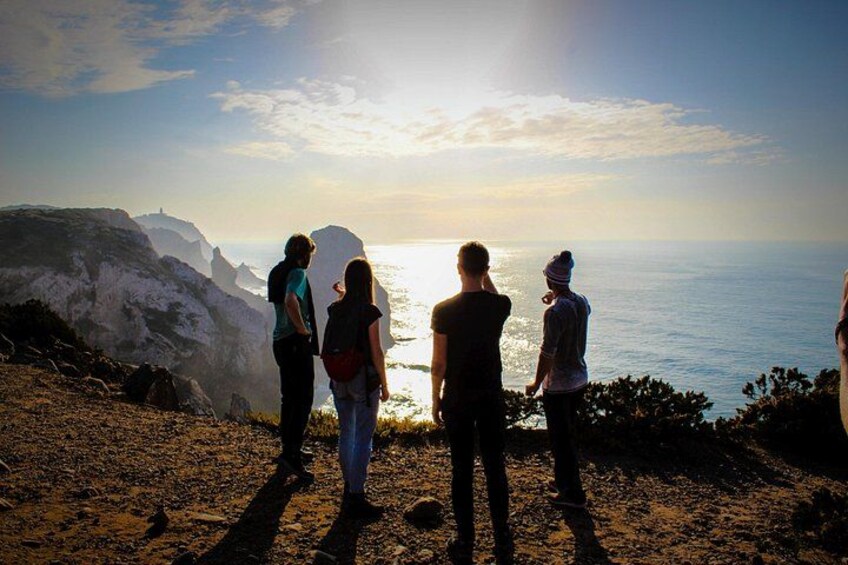 Un groupe de personnes se tient sur une falaise rocheuse, surplombant l’océan au coucher du soleil. 5