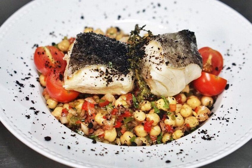 Une assiette blanche contenant un morceau de poisson, des tomates cerises et une salade de pois chiches. 4