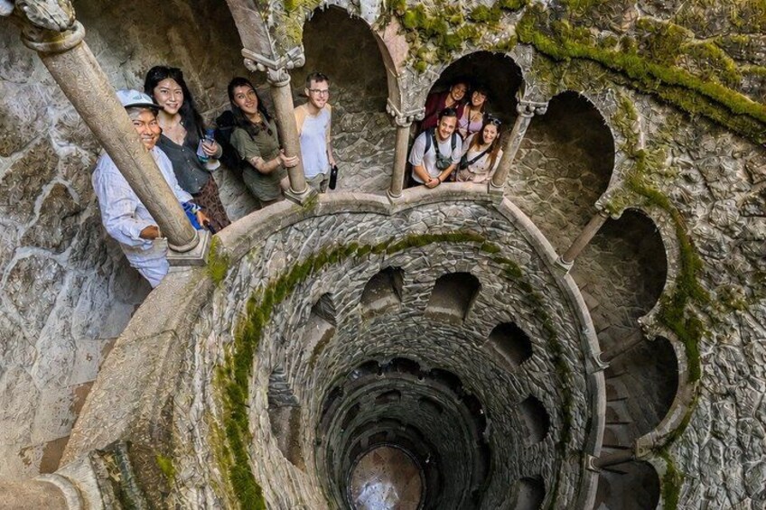 A group of people standing on a stone staircase in a historical building with arches and moss-covered walls. 1