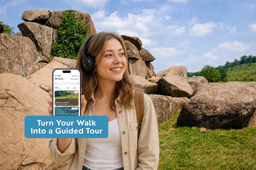 A person holding a smartphone with a travel app interface, standing in front of large rocks and greenery. 3