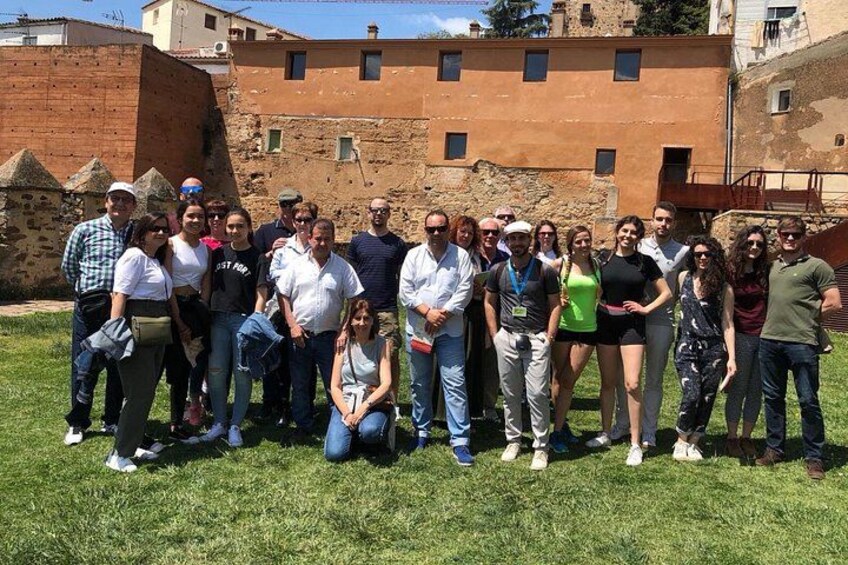 Un gruppo di persone in piedi di fronte a un edificio storico con mura in pietra e un'area verde. 3