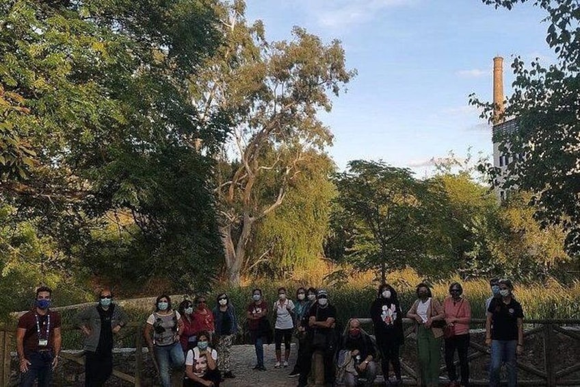 Un gruppo di persone in un parco, sullo sfondo alberi e un camino alto. 4