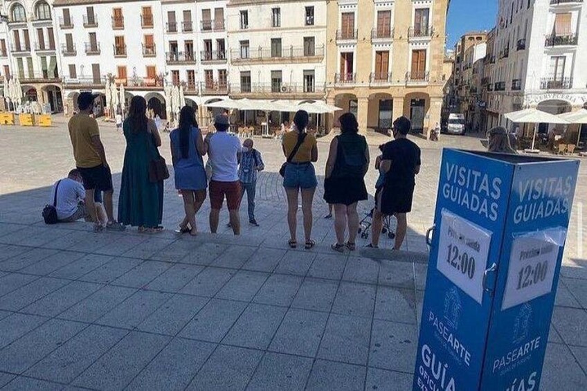 Un gruppo di persone in una piazza, con un cartello che indica visite guidate alle 12:00. 5