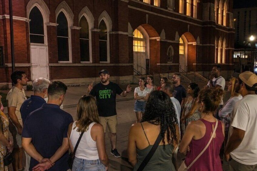 A group of people gathered in front of a building with arched windows and a door. 3