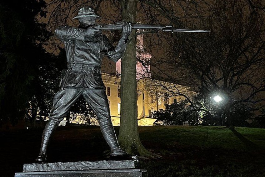 Une statue, visible la nuit, représente un soldat tenant un fusil, avec un arbre et un bâtiment en arrière-plan. 2