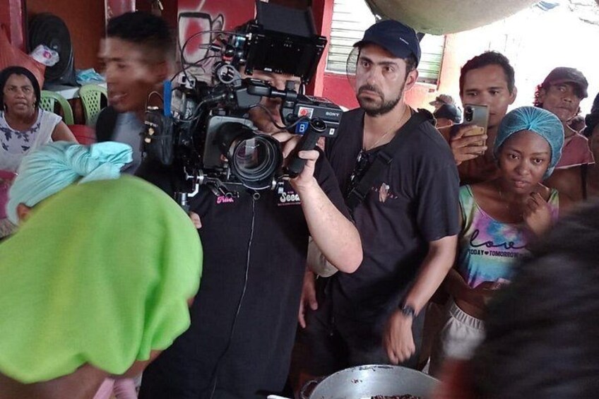 A man with a camera and microphone, surrounded by people. 2