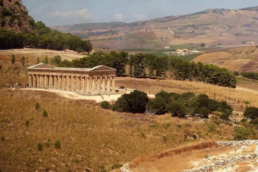 Un templo antiguo con columnas, rodeado de pastizales secos y árboles, con colinas al fondo. 2