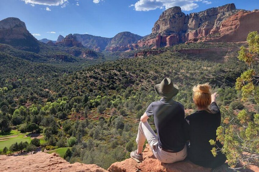 Two people sitting on a rock overlooking a mountainous landscape with a valley below. 4