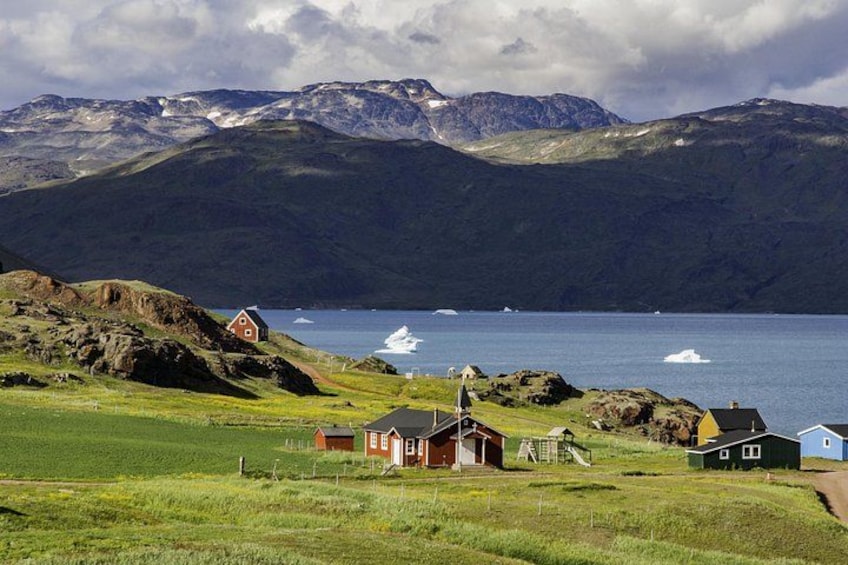 Ett kustlandskap med hus, en kyrka och berg i bakgrunden. 1