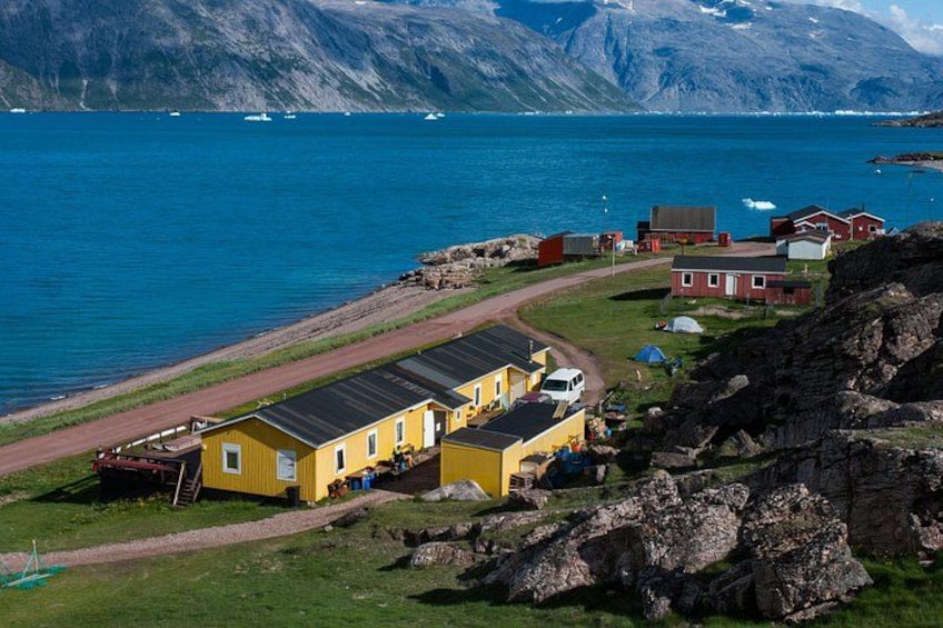 En kustby med gula byggnader, en stenig strand och båtar på vattnet. 3