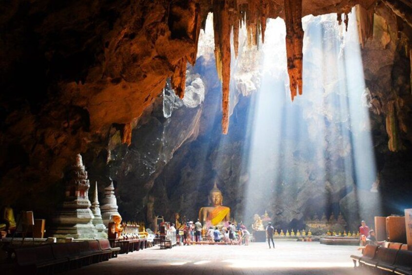 A cave temple with a central Buddha statue, surrounded by smaller stupas and visitors. 1