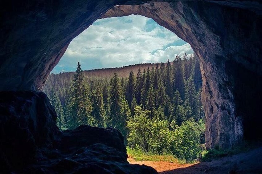 A natural rock arch with a forested landscape visible through it. 2