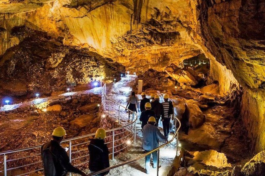 A cave with illuminated paths and visitors wearing hard hats. 1