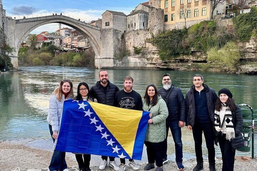 A group of people standing by a river with a bridge in the background. 5
