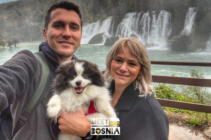 A person holding a small dog with a waterfall in the background. 3