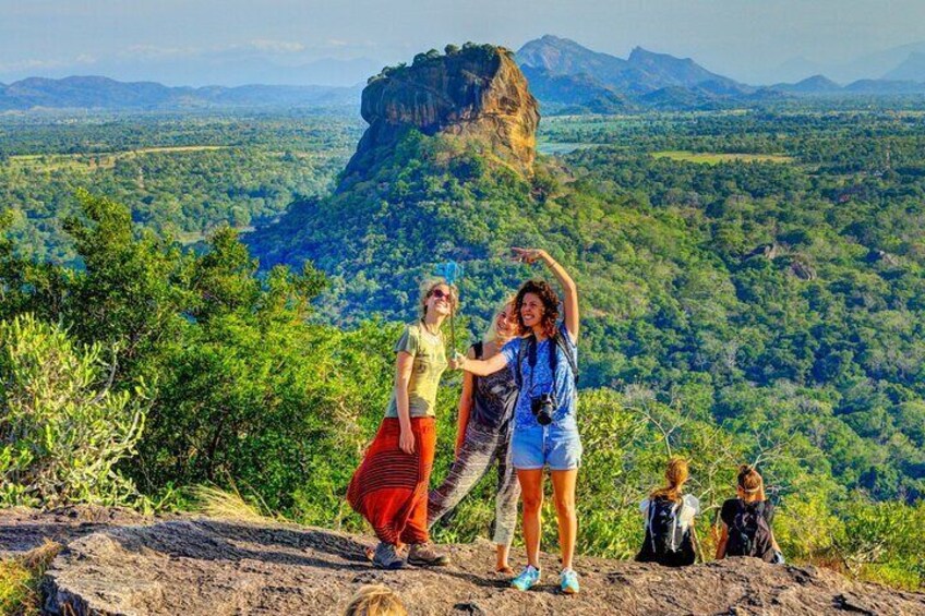 A group of people on a rocky outcrop overlooking a forested valley with a prominent rock formation in the distance. 1