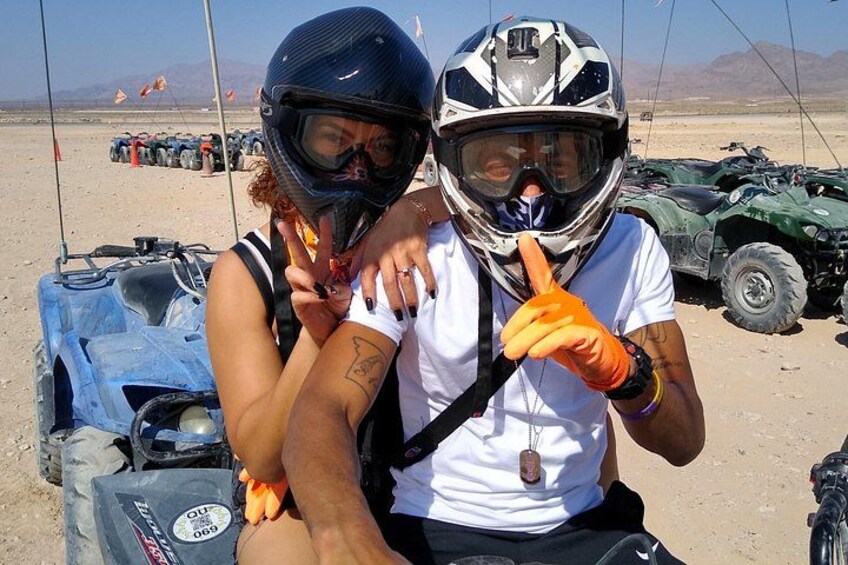 Two people on an ATV in a desert with ATVs and mountains in the background. 5
