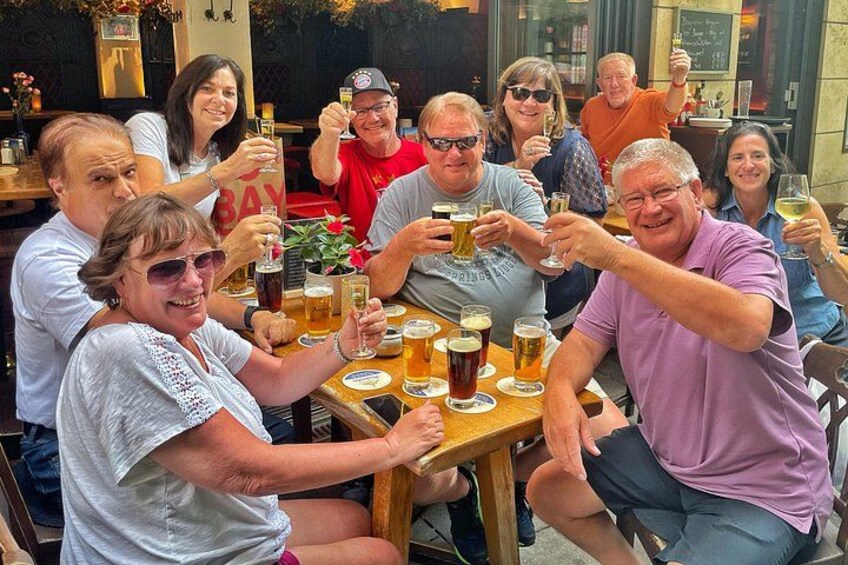 Een groep mensen proost met bierglazen aan een houten tafel buiten. 1