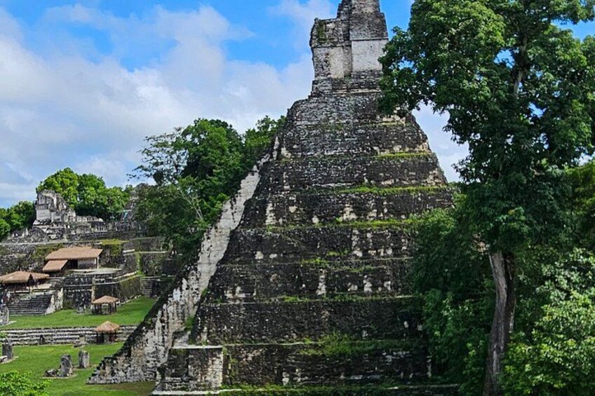Una gran estructura en forma de pirámide rodeada de vegetación exuberante y edificios más pequeños. 3