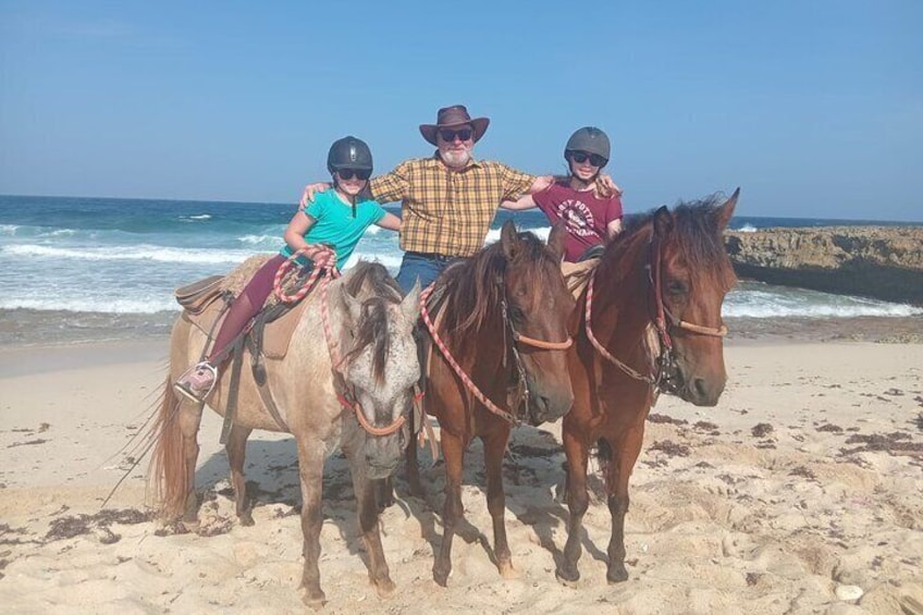 Three people riding horses on a beach with the ocean in the background. 2