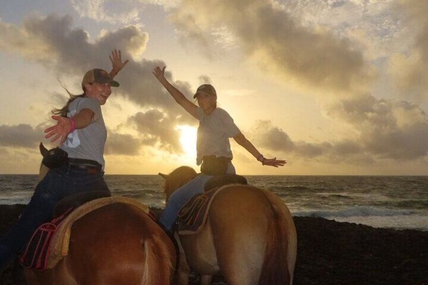 Two people riding horses on a beach with the ocean and a cloudy sky in the background. 4