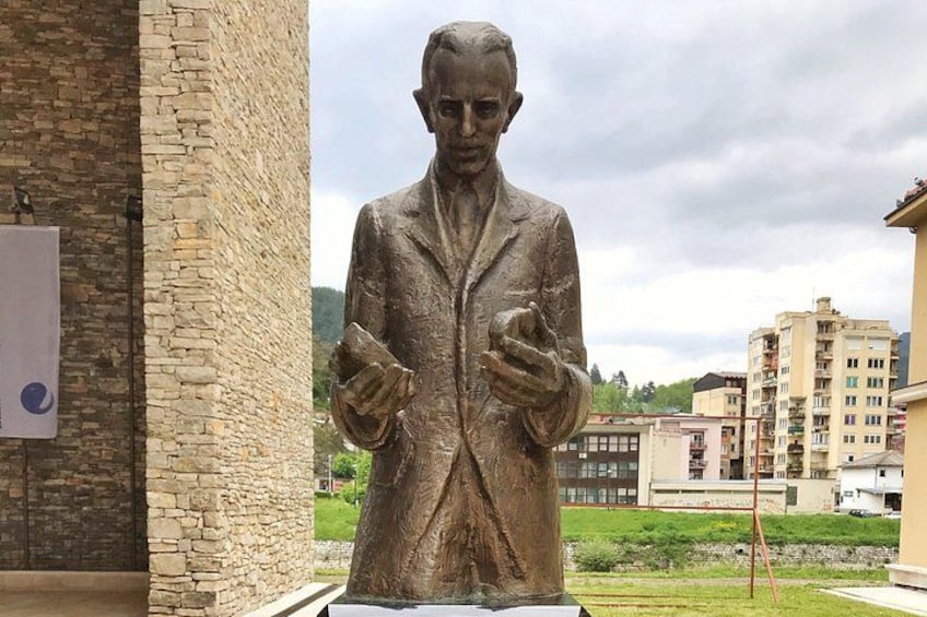 A statue of a man in a suit holding papers, set against a backdrop of buildings and a cloudy sky. 2