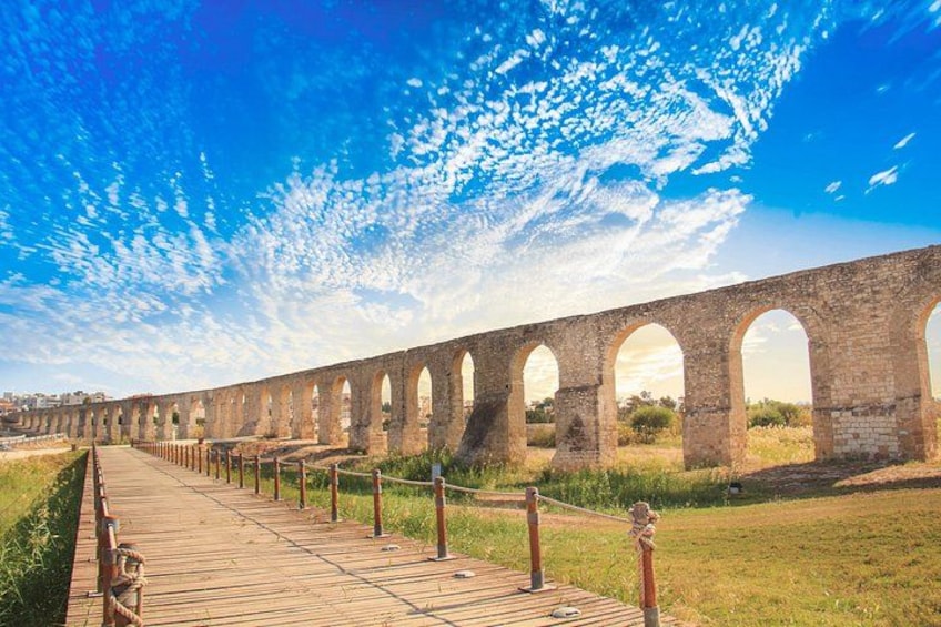 A long stone viaduct with multiple arches, a wooden walkway, and a grassy area. 1