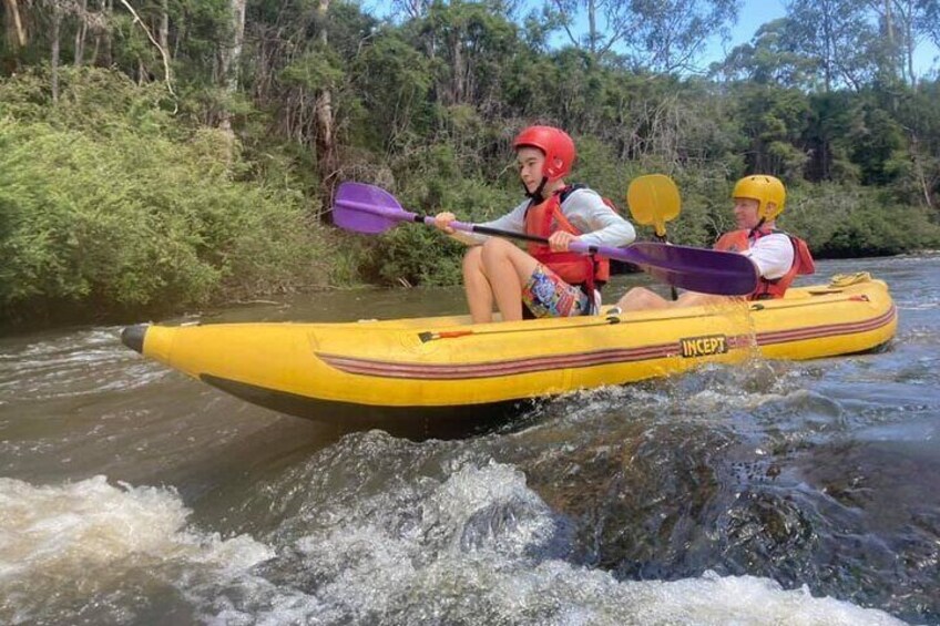 Two people kayaking on a yellow raft in a river surrounded by greenery. 1