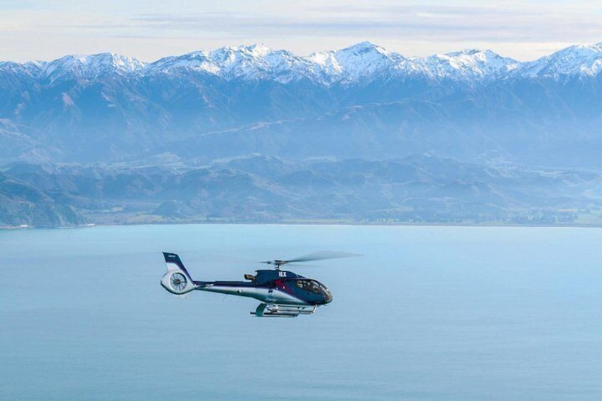 Un hélicoptère survole un lac paisible, avec des montagnes enneigées en arrière-plan. 5