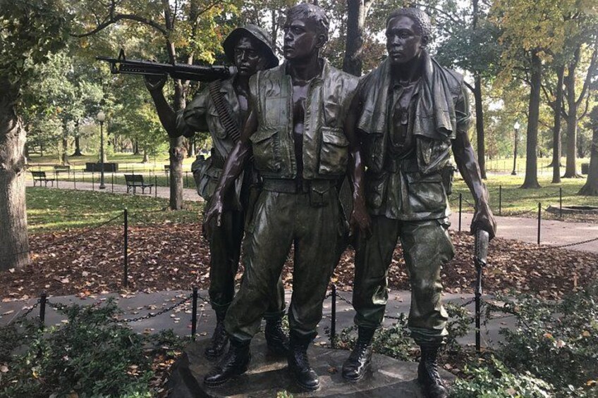 A bronze statue of soldiers in a park with trees and a paved walkway. 3