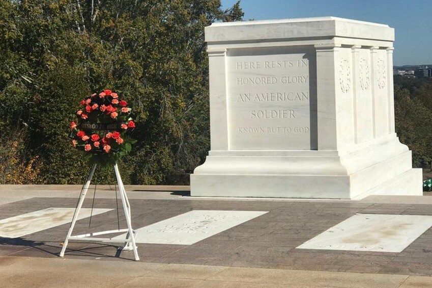 Un monumento commemorativo bianco con iscrizioni, una struttura in metallo bianco e una ghirlanda di fiori rossi. 3